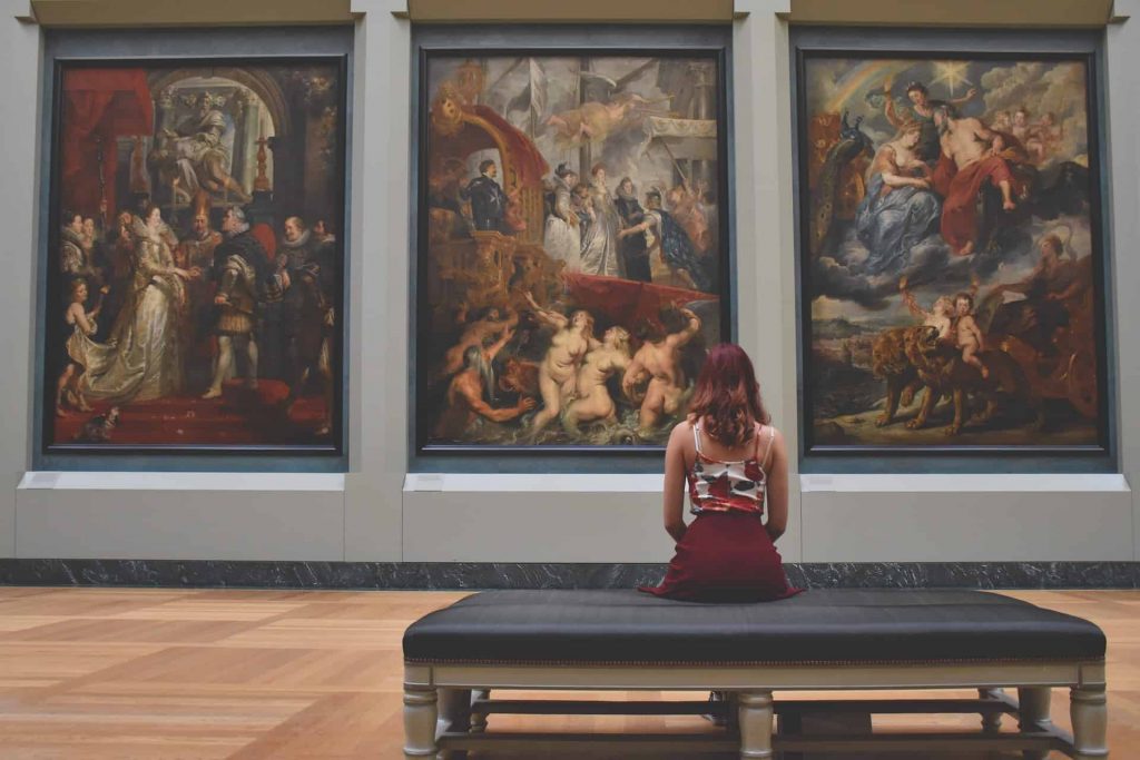 A woman staring at a wall of paintings at a Paris museum