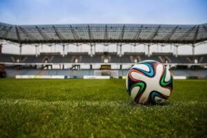 A close up photo of a football on the field with a stadium in the background.