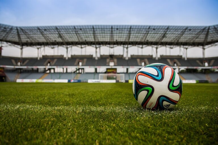 A close up photo of a football on the field with a stadium in the background.