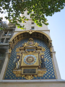 A photo of the oldest clock in Paris. It is gold gilded with a blue background, mounted on a stone wall.