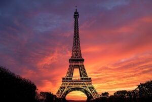 A photo of the Eiffel Tower at sunset. The sky behind it is orange and yellow.