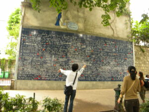 A photo of the Wall of Love in Paris with a person in a white shirt standing in front of it, their arms outstretched.