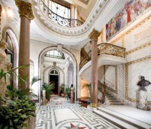 A photo of the interior of the Musee Jacquemart Andre. It shows the hallway leading to the conservatory and the staircase leading to the second floor.