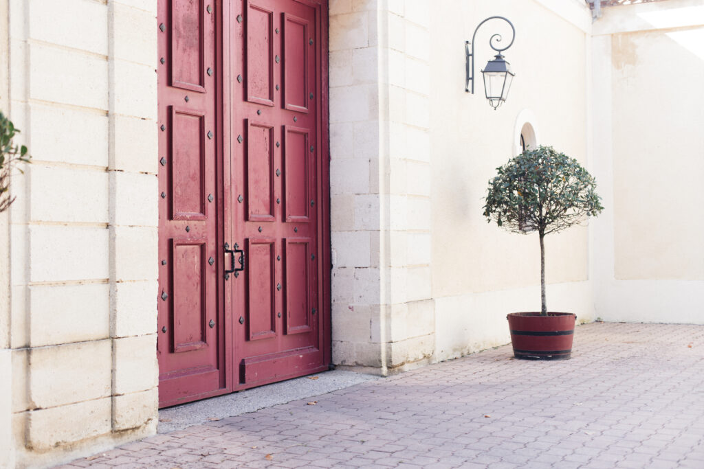 A photo of a door to a building in Paris. The door is red, and there is a planter to the right of it.