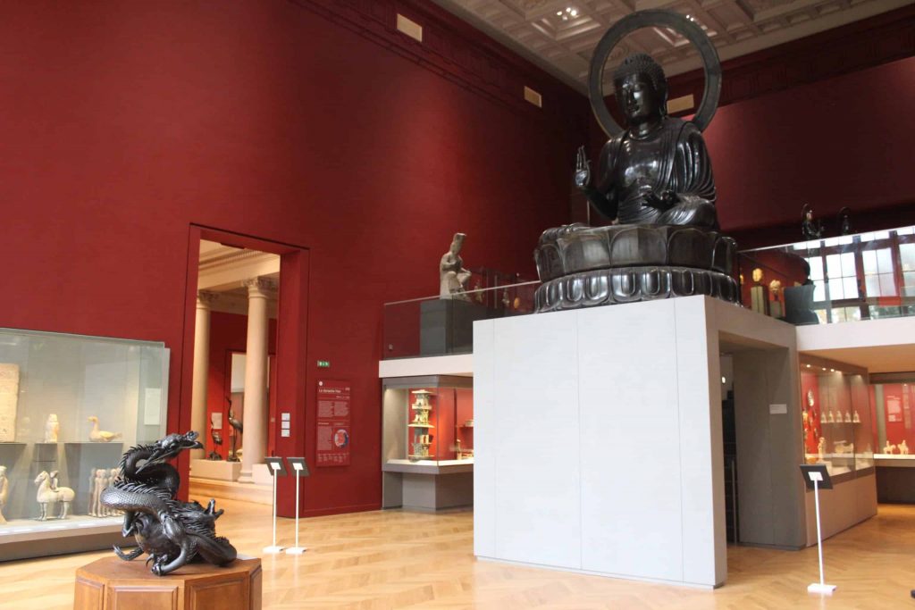 A photo of the great hall of the Musee Cernuschi, with the large Buddha looking down over the incense burner.