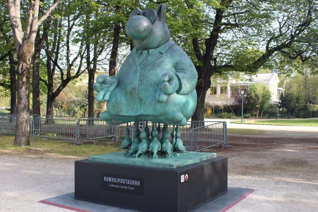 A photo of a bronze sculpture of a large cat sitting crosslegged meditating while a group of birds hold him up with their beaks.