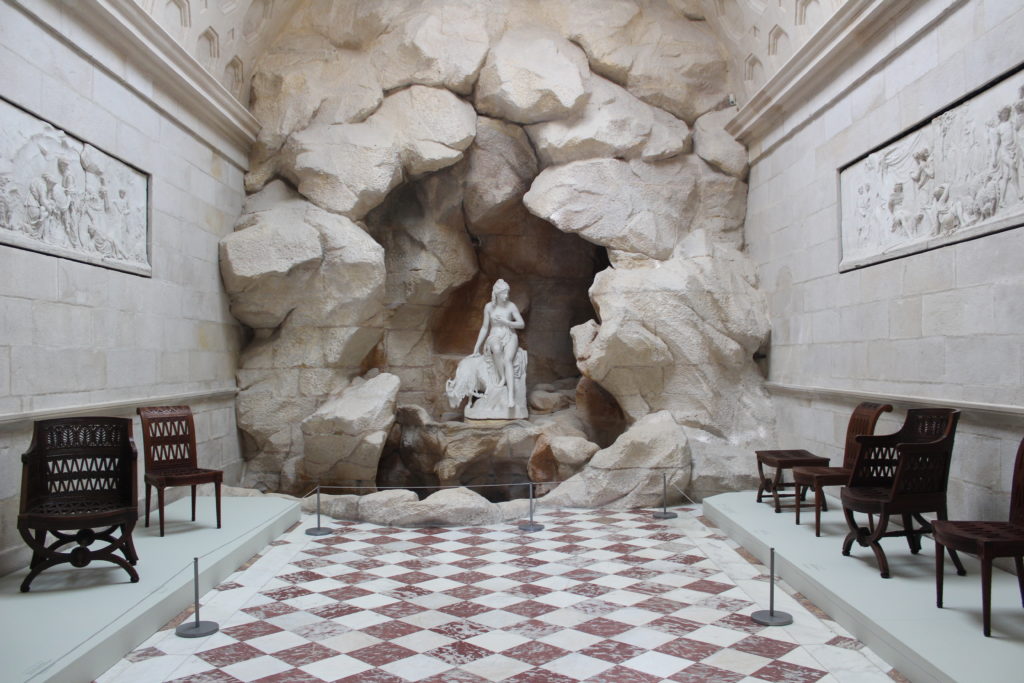 A photo of the Laiterie de la Reine at Château de Rambouillet. The photo is looking down the length of the building to the sculpted grotto and statue at the end.
