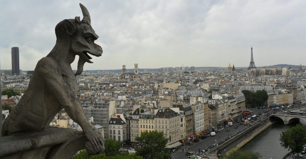 A photo of the view of Paris from the towers of Notre Dame. A gargoyle is in the foreground and the Eiffel Tower is in the distance.