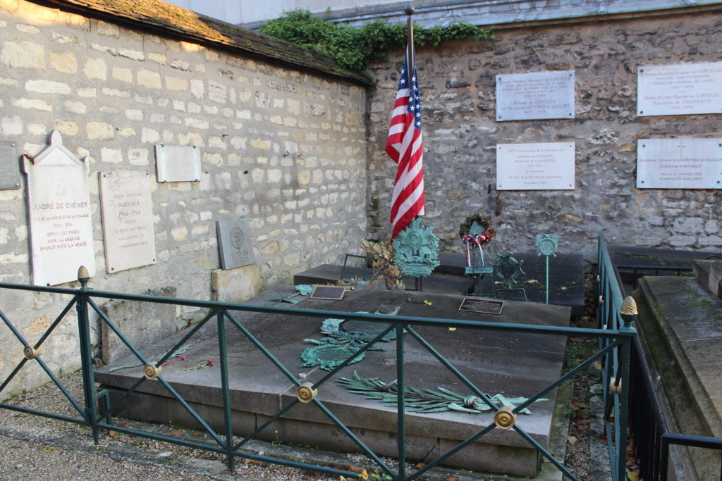 A photo of the grave of the Marquis de Lafayette in the Picpus cemetery. An American flag sits on top of the gravestone.