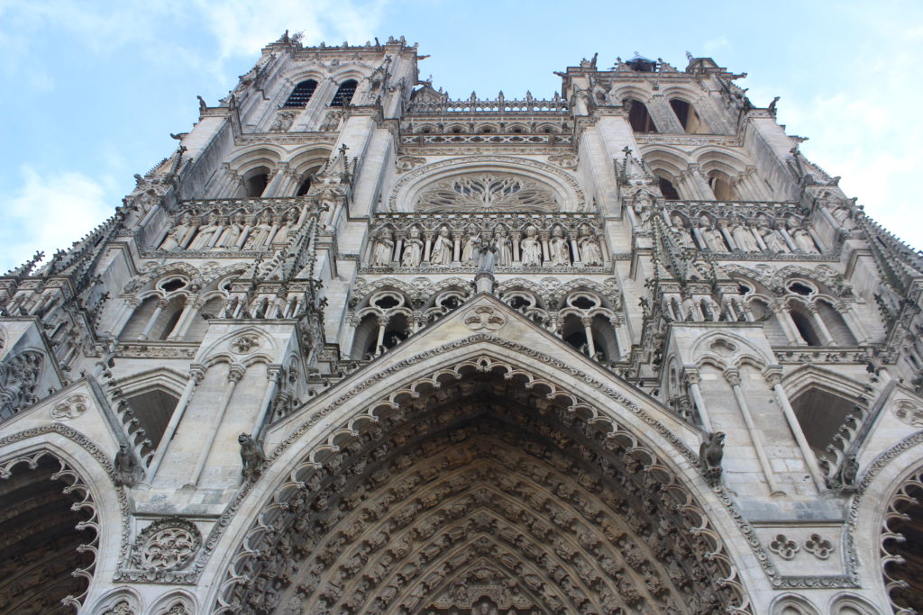 A photo of Amiens Cathedral looking up the western facade. The gallery of kings, the western rose window, and the two towers can be seen.