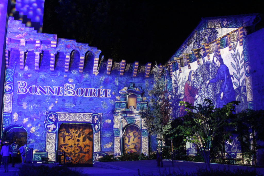 A photo of the Palais des Papes in Avignon. The walls are illuminated with digital images and above the exit door it says "Bonne Soiree".