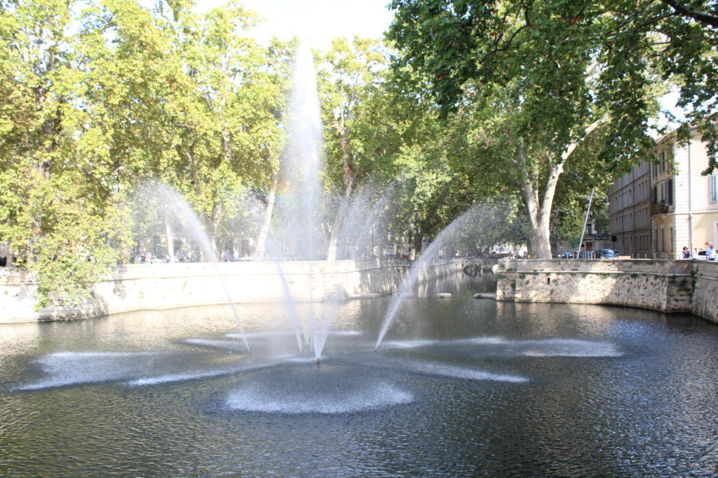 A photo of a fountain in the middle of a canal in Nîmes.