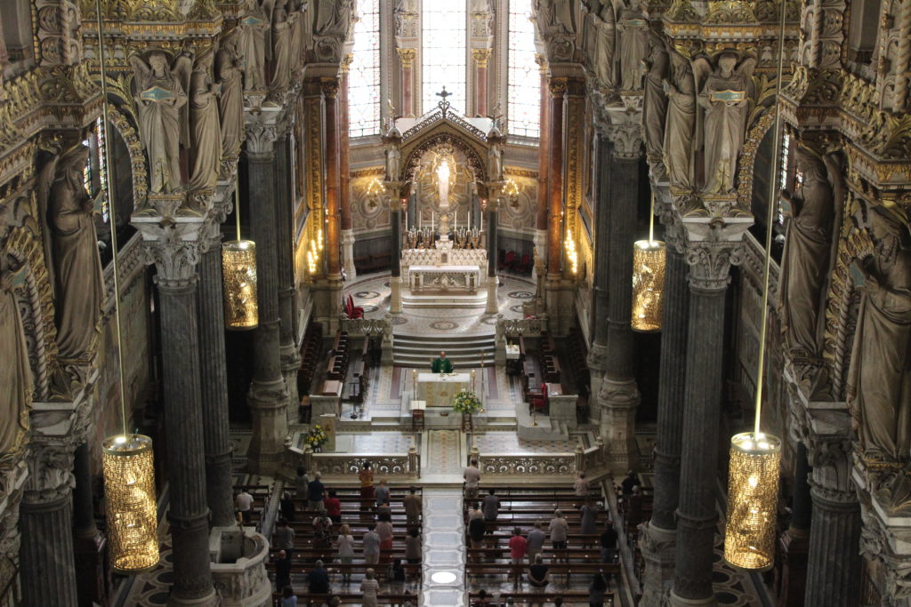 A photo of the interior of the Basilica of Notre-Dame de Fourvière in Lyon. The photo is taken from a great height, looking down the nave towards the altar and apse. 