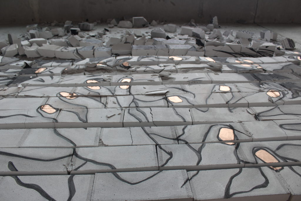 An image of hands painted onto a floor, surrounded by cracked cement blocks.