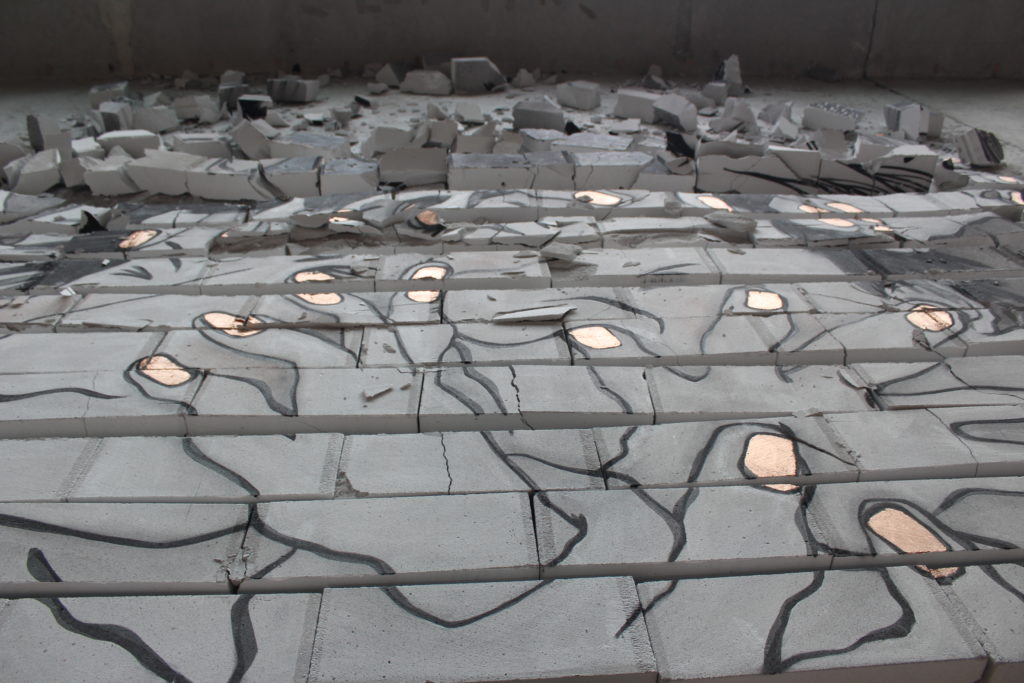 An image of hands painted onto a floor, surrounded by cracked cement blocks.