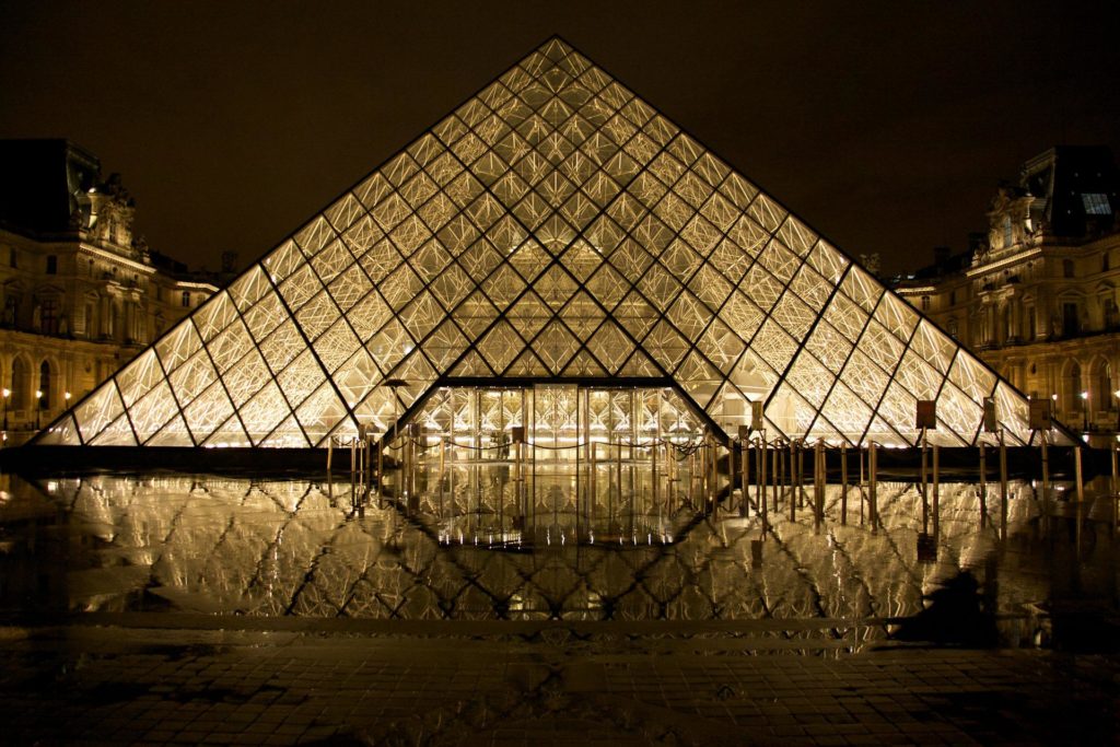A photo of the glass pyramid entrance to the Louvre museum, illuminated at night.