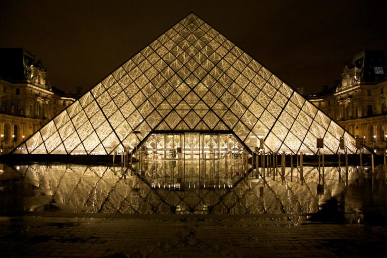 A photo of the glass pyramid entrance to the Louvre museum, illuminated at night.