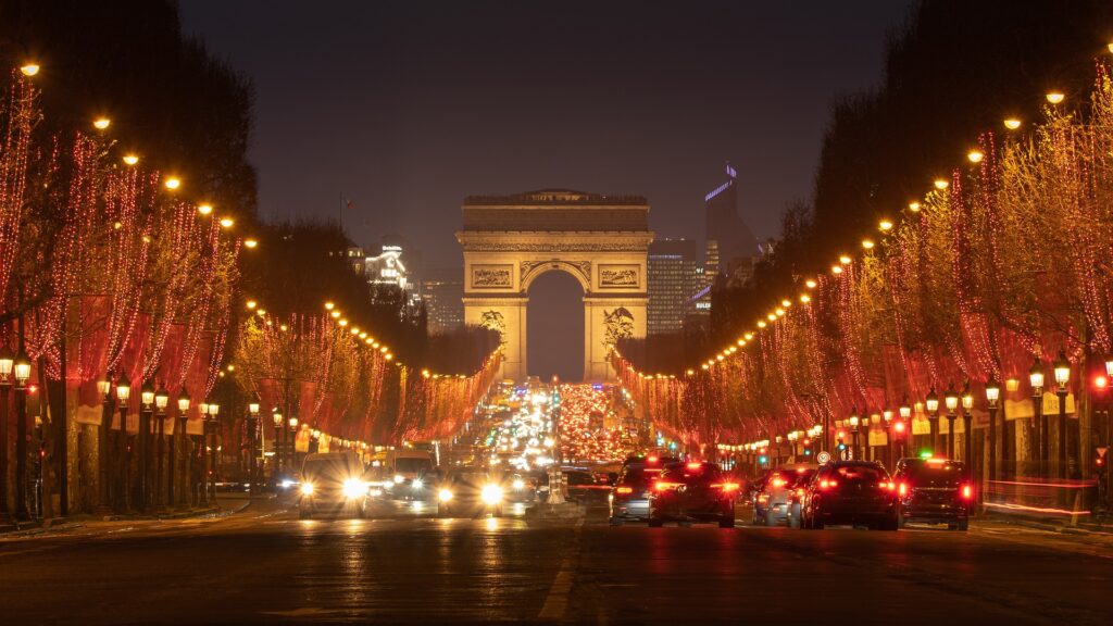 A photo of the Champs Élysées looking up towards the Arc de Triomphe. Christmas lights illuminate either side of the boulevard.