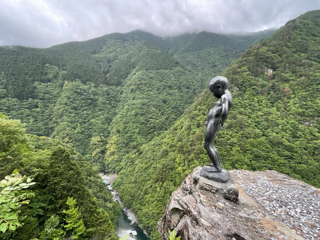 A photo of the peeing boy statue overlooking a gorge in Iya Valley, Japan.