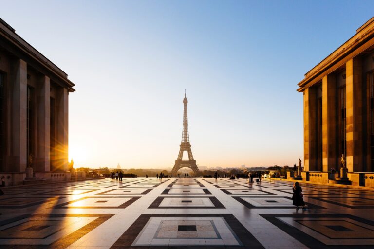 A photo of the plaza at Trocadero in the 16e arrondissement of Paris. It is sunrise, and the Eiffel Tower can be seen in the distance.