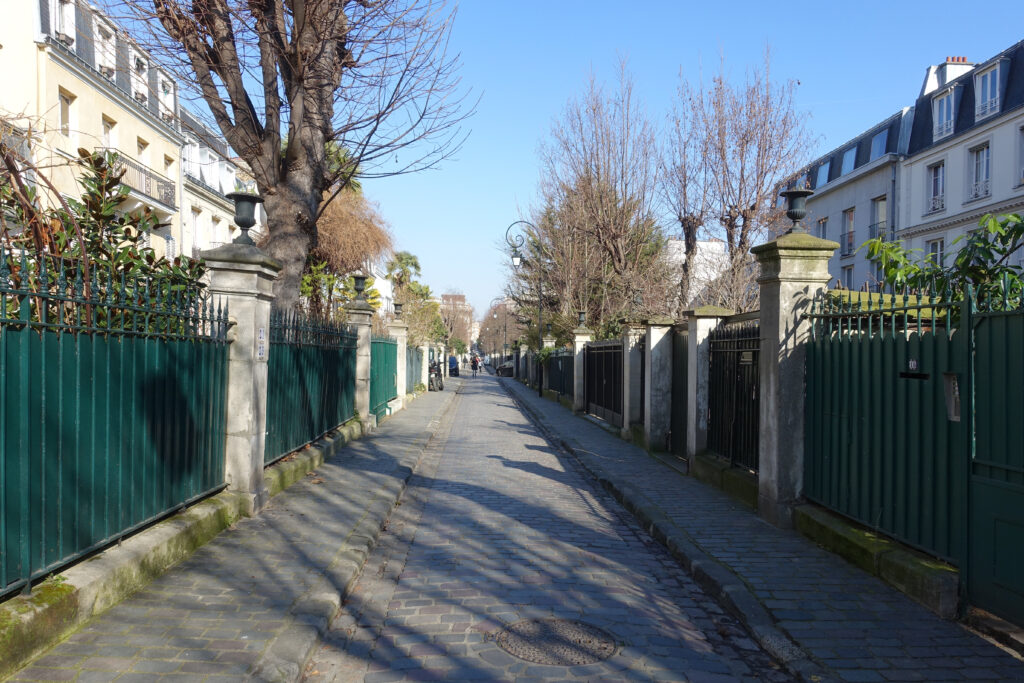 A photo of Cite des Fleurs street in the 17e arrondissement. It shows a narrow, pedestrian road, lined with gates and houses.