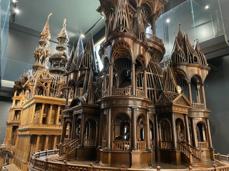 A photo of the wooden structures on display in the Aux arts et sciences réunis museum in the 19e. The pieces are wooden scale models of intricate castles and religious buildings.