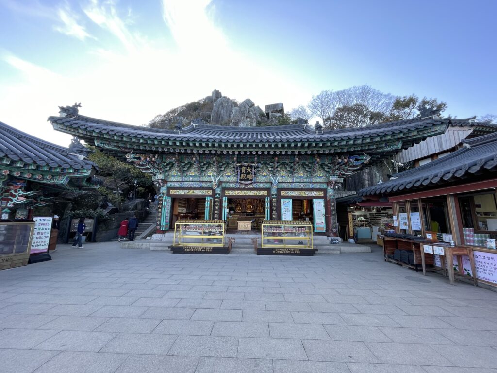 A photo of Hyangiram Temple in Yeosu South Korea. It shows the facade of the main building of the temple, with the mountains in the background.