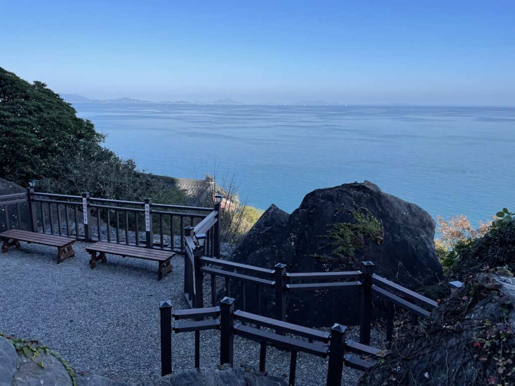 A photo of a resting area in Hyangiram Temple where you can reflect on travel magic. There are two benches with a fence in front of them, and a magnificent view of the ocean in front of them.