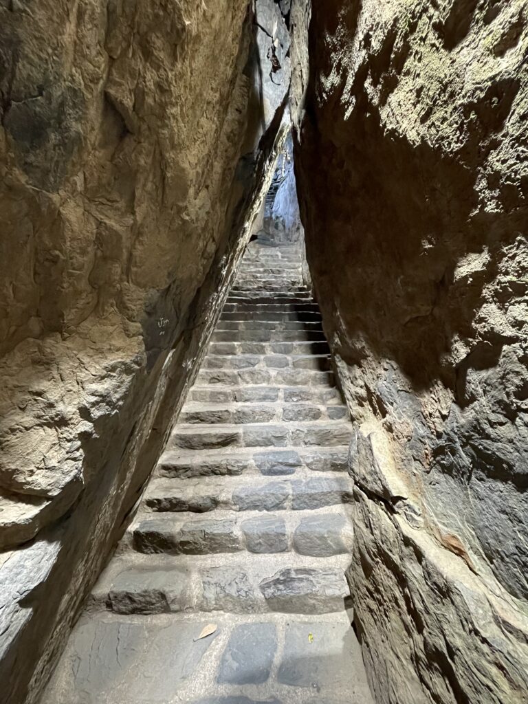 A photo of a flight of stone steps with high rock walls on either side that come to a point above the stairs, forming a tunnel for climbers.