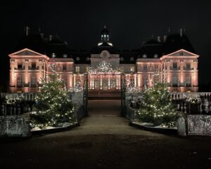 A photo of the front facade of Vaux-Le-Vicomte. It is nighttime, and the facade is illuminated with lights.